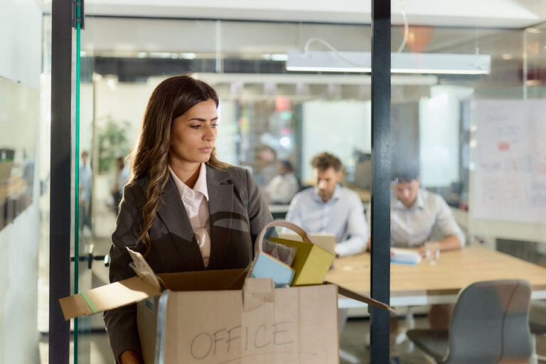 Eine Frau verlässt mit einem Karton ein Büro